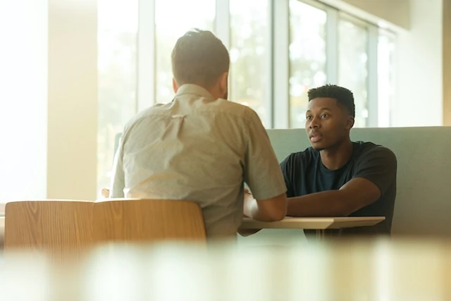 Two men sitting at a table looking at each other with natural sun light