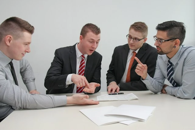 Group of people sitting at a desk looking at paper sheets with unnatural conversation
