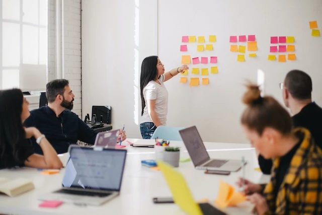 Group of people in a creative meeting room looking at a whiteboard with sticky notes
